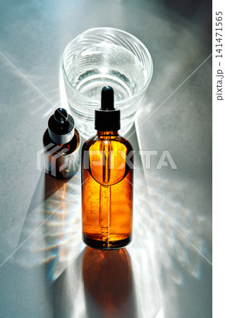 Skincare serum bottles with glass of water and sunlight 141471565