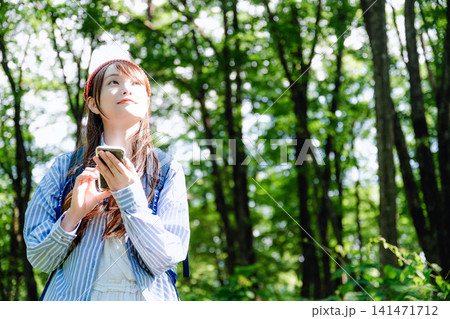 木漏れ日の森でスマートフォンを持つ女性 木漏れ日の森でスマートフォンを持つ女性 141471712