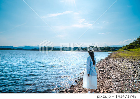 夏の日差しの中で湖の水辺に佇む女性 夏の日差しの中で湖の水辺に佇む女性 141471748