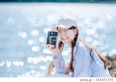 水辺でフィルムカメラを持つ白い帽子の女性 水辺でフィルムカメラを持つ白い帽子の女性 141471773
