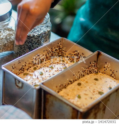 Artisan Bread Dough in Loaf Pans Topped with Mixed Seeds During Baking Preparation, Homemade Whole Grain Bread Process in Bakery Kitchen, Close Up Food Preparation Scene 141472031