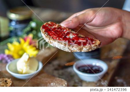Hand Holding Rustic Artisan Bread with Berry Jam, Homemade Breakfast Toast with Butter, Fresh Whole Grain Bread, Healthy Morning Meal, Bakery Lifestyle Food Photography 141472396
