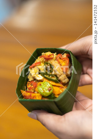 Hand Holding Traditional Indonesian Rice Meal in Banana Leaf Takir with Assorted Toppings, Authentic Nusantara Cuisine, Eco Friendly Food Packaging, Homemade Asian Culinary Hand Holding Traditional Indonesian Rice Meal in Banana Leaf Takir with Assorted Toppings, Authentic Nusantara Cuisine, Eco Friendly Food Packaging, Homemade Asian Culinary 141472532