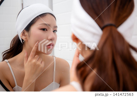 Beautiful young asian woman examining skin of facial while looking mirror in bathroom at home. Beautiful young asian woman examining skin of facial while looking mirror in bathroom at home. 141472563