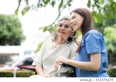 Young caucasian nurse comforting with patient while sitting on wheelchair in outdoor park. Young caucasian nurse comforting with patient while sitting on wheelchair in outdoor park. 141474274