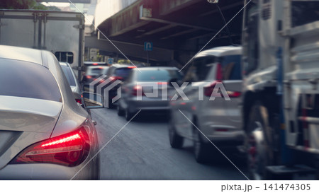 Rear perspective view of multiple vehicles queuing in traffic near an elevated highway structure. Bright daylight illuminates the urban commuting scene. Heavy traffic during rush hour. Rear perspective view of multiple vehicles queuing in traffic near an elevated highway structure. Bright daylight illuminates the urban commuting scene. Heavy traffic during rush hour. 141474305