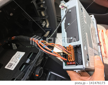 Car radio unit with orange wiring connector partially installed in the dashboard. 141476173
