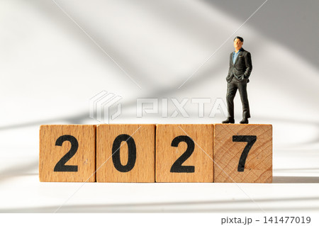 Miniature Businessman Standing on Wooden 2027 Blocks Symbolizing Success and New Year Goals Miniature Businessman Standing on Wooden 2027 Blocks Symbolizing Success and New Year Goals 141477019