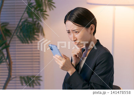 スマホを見て悩むスーツの女性 スマホを見て悩むスーツの女性 141478558
