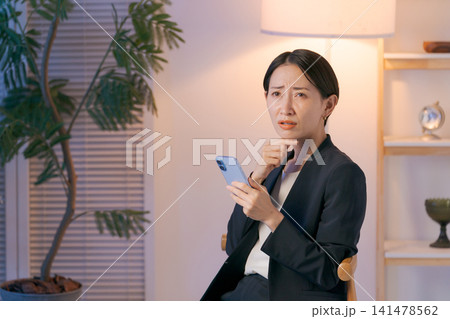 スマホを見て悩むスーツの女性 141478562