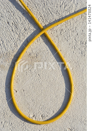 Yellow electric cable loop on textured plaster wall background 141478824
