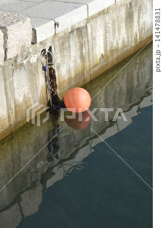 Orange mooring buoy floating by concrete stone dock wall Orange mooring buoy floating by concrete stone dock wall 141478831