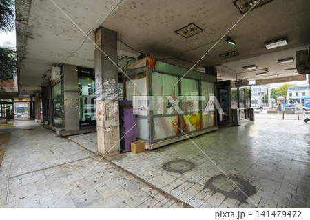 pedestrian walkway beneath a dirty concrete overhang features abandoned storefronts and kiosks. in Podgorica, Montenegro pedestrian walkway beneath a dirty concrete overhang features abandoned storefronts and kiosks. in Podgorica, Montenegro 141479472