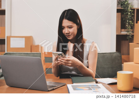 Startup SME small business entrepreneur of freelance Asian woman wearing apron using laptop and box to receive and review orders online to prepare to pack sell to customers, online sme business ideas. Startup SME small business entrepreneur of freelance Asian woman wearing apron using laptop and box to receive and review orders online to prepare to pack sell to customers, online sme business ideas. 141480718
