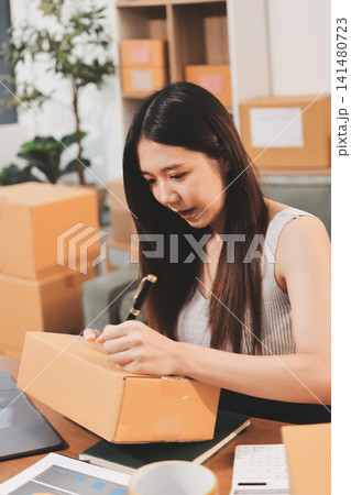 Startup SME small business entrepreneur of freelance Asian woman wearing apron using laptop and box to receive and review orders online to prepare to pack sell to customers, online sme business ideas. Startup SME small business entrepreneur of freelance Asian woman wearing apron using laptop and box to receive and review orders online to prepare to pack sell to customers, online sme business ideas. 141480723