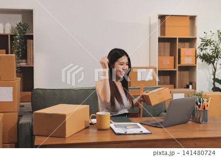 Startup SME small business entrepreneur of freelance Asian woman wearing apron using laptop and box to receive and review orders online to prepare to pack sell to customers, online sme business ideas. Startup SME small business entrepreneur of freelance Asian woman wearing apron using laptop and box to receive and review orders online to prepare to pack sell to customers, online sme business ideas. 141480724