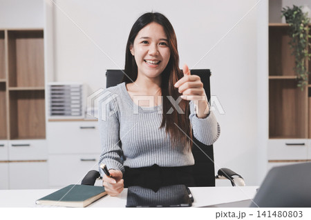 young woman is working on laptop in modern office environment, showcasing focused and productive atmosphere. She is dressed in professional white shirt, with coffee cup and small plant on table, young woman is working on laptop in modern office environment, showcasing focused and productive atmosphere. She is dressed in professional white shirt, with coffee cup and small plant on table, 141480803