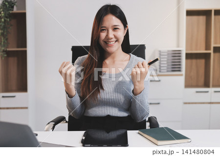 young woman is working on laptop in modern office environment, showcasing focused and productive atmosphere. She is dressed in professional white shirt, with coffee cup and small plant on table, young woman is working on laptop in modern office environment, showcasing focused and productive atmosphere. She is dressed in professional white shirt, with coffee cup and small plant on table, 141480804