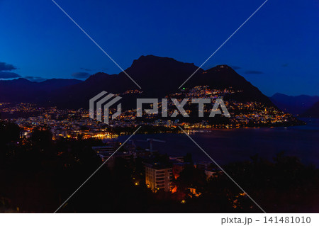 スイス・ルガーノの夜景全景、湖を囲む街の灯りと山のシルエット 141481010