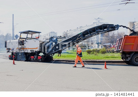 UKRAINE. KYIV - 19.03.2021. Road construction working. The road milling machine removes old asphalt and loads milled asphalt into the dump truck. Road repair process UKRAINE. KYIV - 19.03.2021. Road construction working. The road milling machine removes old asphalt and loads milled asphalt into the dump truck. Road repair process 141481441