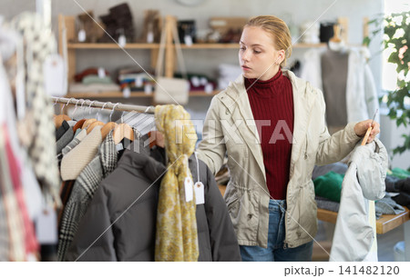 Attentive teenage girl choosing lightweight jacket in clothing store Attentive teenage girl choosing lightweight jacket in clothing store 141482120