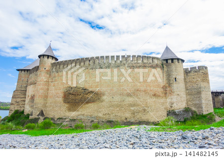 View of old castle Hotin near the river. Khotyn Fortress - medieval castle on yellow autumn hills. Ukraine, Eastern Europe. The architecture of the Middle Ages in our time. 141482145
