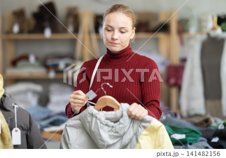 While shopping, teen girl browsing goods items and choose elect down jacket in store While shopping, teen girl browsing goods items and choose elect down jacket in store 141482156
