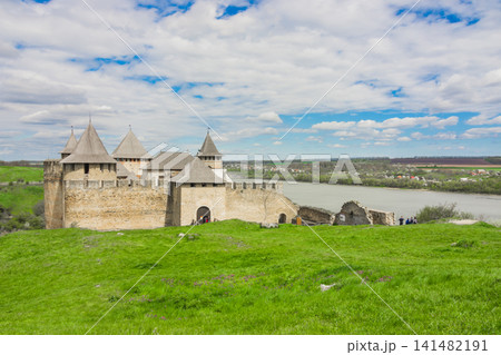 View of old castle Hotin near the river. Khotyn Fortress - medieval castle on yellow autumn hills. Ukraine, Eastern Europe. The architecture of the Middle Ages in our time. View of old castle Hotin near the river. Khotyn Fortress - medieval castle on yellow autumn hills. Ukraine, Eastern Europe. The architecture of the Middle Ages in our time. 141482191