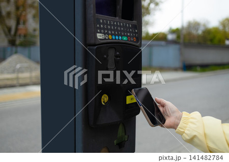 Close up of hand making contactless smartphone payment at city parking meter. 141482784
