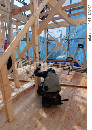 Construction Worker Carrying Timber Beam Inside Wooden House Frame Under Construction Construction Worker Carrying Timber Beam Inside Wooden House Frame Under Construction 141483200