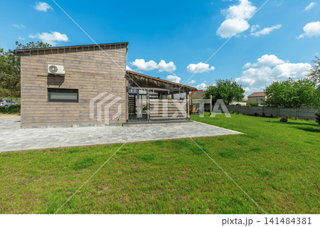 Modern Wooden House Exterior with Paved Patio and Lawn 141484381