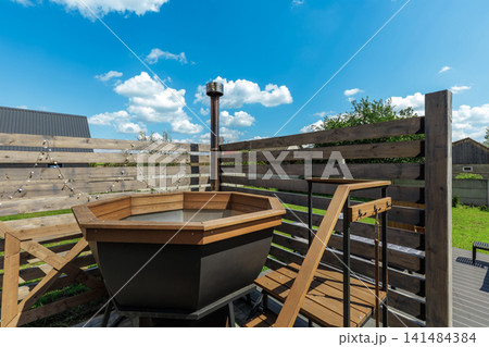 Wooden Hot Tub with Chimney and Steps Against Blue Sky 141484384