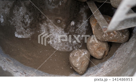 Inside worn metal, wet stones rest in muddy residue beside white dust and rust marks, creating rough industrial texture from heavy building material on construction site Inside worn metal, wet stones rest in muddy residue beside white dust and rust marks, creating rough industrial texture from heavy building material on construction site 141486953