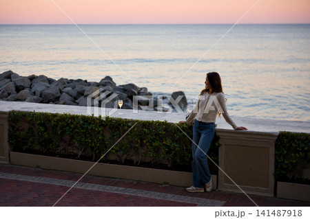 Woman Looking At Ocean From A Seaside Wall At Sunset Woman Looking At Ocean From A Seaside Wall At Sunset 141487918