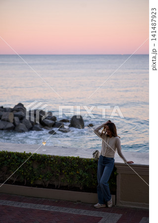 Woman Gazes At The Sea While Standing Along A Coastal Wall Woman Gazes At The Sea While Standing Along A Coastal Wall 141487923