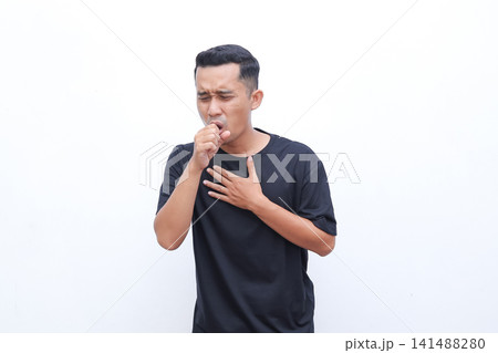 Man coughs, holding hand to throat. He wears a simple black T-shirt. Background is plain white, clean and bright. His expression shows discomfort or illness. Ideal for health, wellness Man coughs, holding hand to throat. He wears a simple black T-shirt. Background is plain white, clean and bright. His expression shows discomfort or illness. Ideal for health, wellness 141488280