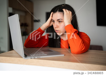Frustrated young woman holding her head while looking at a laptop screen indoors. Stress management digital burnout and workplace challenges Frustrated young woman holding her head while looking at a laptop screen indoors. Stress management digital burnout and workplace challenges 141488803