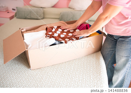 Woman organizing clothes in cardboard box on bed with soft bedding Woman organizing clothes in cardboard box on bed with soft bedding 141488836