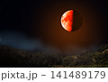 Eclipse - Blood moon with orange surface over forest at night. Half of the moon is illuminated. 141489179