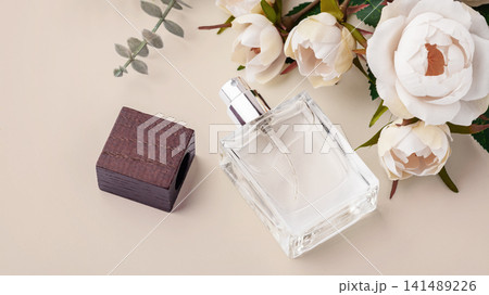 Perfume bottle with wooden cap with blooming floral decorations on a pastel beige background 141489226