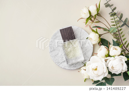 Perfume bottle with wooden cap on marble tray with white roses decoration on beige background, top view Perfume bottle with wooden cap on marble tray with white roses decoration on beige background, top view 141489227