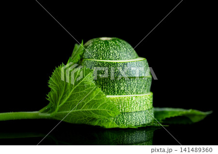 Raw zucchini with yellow flower and foliage on black studio background Raw zucchini with yellow flower and foliage on black studio background 141489360