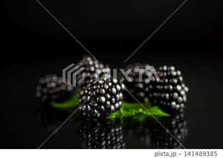 Minimal blackberry arrangement with fresh green leaves on black backdrop 141489385