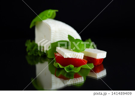 Fresh feta cheese with tomato and basil on black background Fresh feta cheese with tomato and basil on black background 141489409