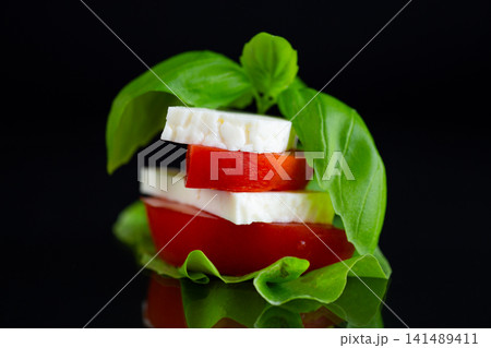 Fresh Mediterranean cheese with basil leaves on elegant black background Fresh Mediterranean cheese with basil leaves on elegant black background 141489411