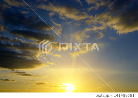 Majestic Sunrise Sky with Bright Sun Rays and Dramatic Fluffy Clouds. Beautiful Golden Light Illuminating Dark Blue Skyscape Background with Copy Space. Majestic Sunrise Sky with Bright Sun Rays and Dramatic Fluffy Clouds. Beautiful Golden Light Illuminating Dark Blue Skyscape Background with Copy Space. 141489581