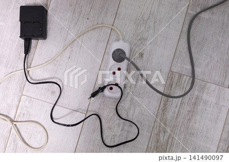 Top view of extension cord, power adapter and tangled electrical cables connected on a wooden floor, illustrating everyday household electricity use and home workspace setup Top view of extension cord, power adapter and tangled electrical cables connected on a wooden floor, illustrating everyday household electricity use and home workspace setup 141490097