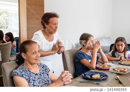 Hispanic family women and girl praying before meal at dining table Hispanic family women and girl praying before meal at dining table 141490393