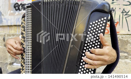 Male hands of musician playing the accordion at urban street. The detailed view highlights texture of instrument, capturing rhythm, tradition, and the expressive character of live music performance Male hands of musician playing the accordion at urban street. The detailed view highlights texture of instrument, capturing rhythm, tradition, and the expressive character of live music performance 141490514
