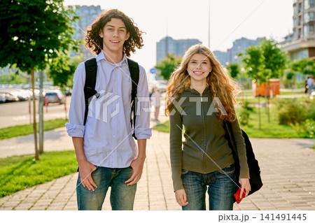 Two happy diverse teenager students with backpacks standing outside on a sunny city street Two happy diverse teenager students with backpacks standing outside on a sunny city street 141491445